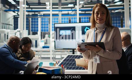 Portrait of smiling scientist in factory using tablet to check PV materials parameters, improving solar panels. Happy researcher develops efficient sustainable energy solutions using device, camera A Stock Photo