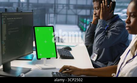 Programmers use isolated screen tablet in server room, developing disaster recovery plans ensuring minimal downtime. Data center employee looking at chroma key device, monitoring performance, camera A Stock Photo