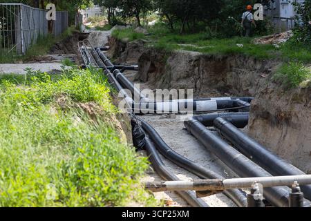 Worker in protective helmet and uniform supervising installation of underground water pipes in deep trench. Hard physical labor and utility repair Stock Photo