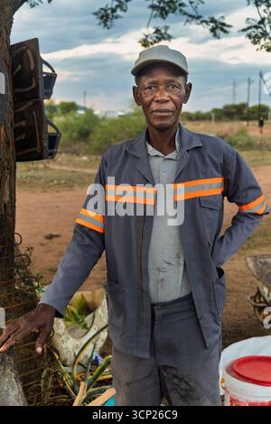 africa village, portrait of single happy african elderly man, standing on a dirt road, next to a fire, garbage around Stock Photo