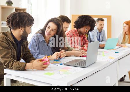 Team of young diverse people working in office, discussing ideas, and using laptops Stock Photo