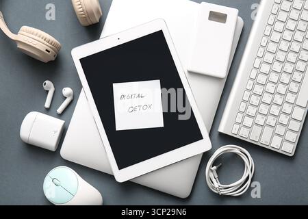 Sticky note with text DIGITAL DETOX and different modern gadgets on dark background Stock Photo