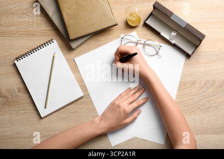 Female hands with blank paper sheets, fountain pen, stationery and books on wooden background Stock Photo