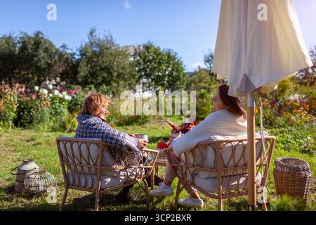 Family having coffee drinks in fall garden. Mother and daughter relaxing on outdoor furniture covered with blankets. Breakfast on terrace with autumn Stock Photo