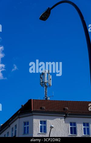 Vertical image of 5G cellular antenna (5G Mast) on urban rooftop in Berlin with curved streetlight in foreground, clear blue sky background. Stock Photo