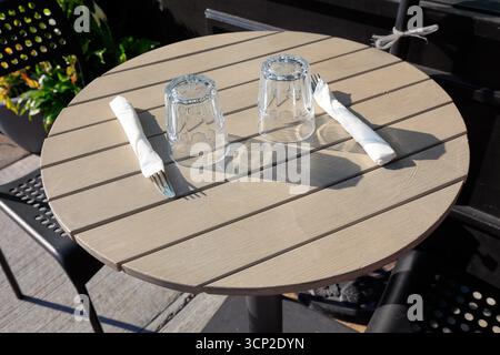 A simple table setting consisting of a water glass, fork and knife on an outdoor cafe table. Stock Photo