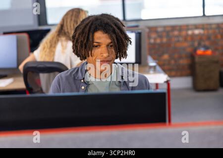 Diverse coworkers working at desks with monitors, keyboards and mouse in open plan office Stock Photo