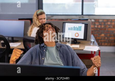 Diverse coworkers celebrating success in open-plan office at desks with monitors and documents Stock Photo