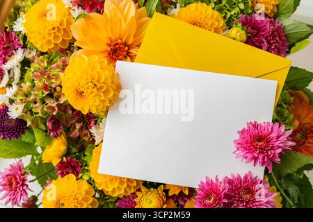 Empty white paper note copy space with yellow envelope Autumn garden colorful flowers. Beautiful autumnal bouquet dahlia chrysanthemum. Red pink orange fall color fall floral background. Flower shop and florist design concept idea Stock Photo