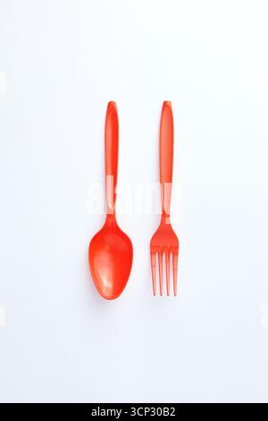 A red plastic spoon and fork are placed side by side on a clean white background, creating a simple and minimalistic composition Stock Photo