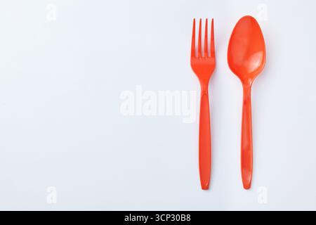 Red plastic spoons and forks are placed side by side on a clean white background, creating a simple and minimalist unbalanced composition. Stock Photo