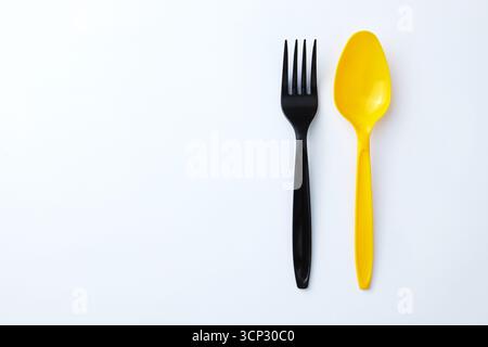 A black plastic fork next to a yellow plastic spoon on a white background Stock Photo