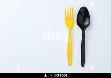A yellow plastic fork next to a black plastic spoon on a white background Stock Photo