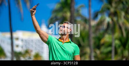 Tourist takes a selfie near palm tree. Man captures a selfie during summer vacation. Traveler snaps a selfie in a tropical destination. A selfie with Stock Photo