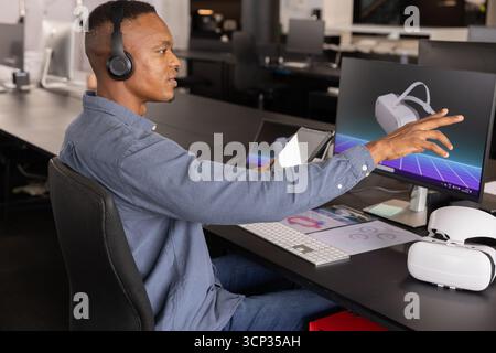 Mid adult african american man in headphones using tablet at desk at office with vr headset Stock Photo