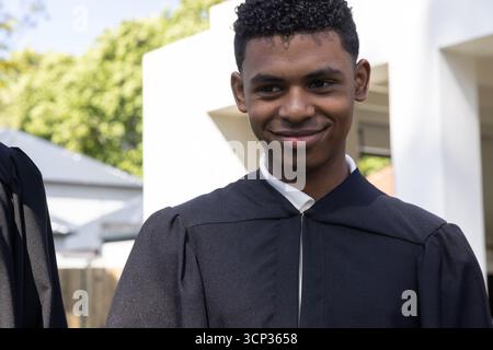 African american male student standing in courtyard wearing black gown over shirt by columns Stock Photo