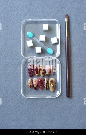 Top view of bold and artistic 3D nail art set with brush, sponge stick, and foam cubes on gray background. Creative concept for nail fashion and beaut Stock Photo