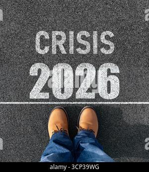 A person in boots and jeans stands on a white line on asphalt, with the words CRISIS 2026 written in front of them Stock Photo