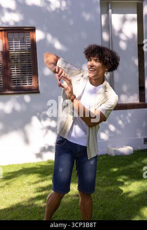 Sunlight is casting tree-shadow patterns across white stucco house wall over grass lawn Stock Photo