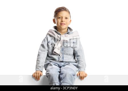Cute boy in jeans sitting on a blank panel isolated on white background Stock Photo