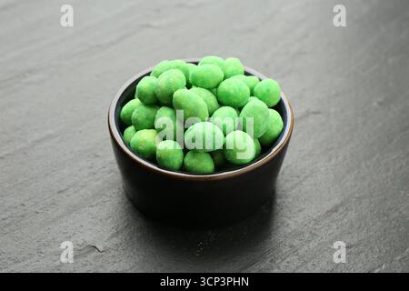 Delicious wasabi coated peanuts in bowl on dark textured table, closeup Stock Photo
