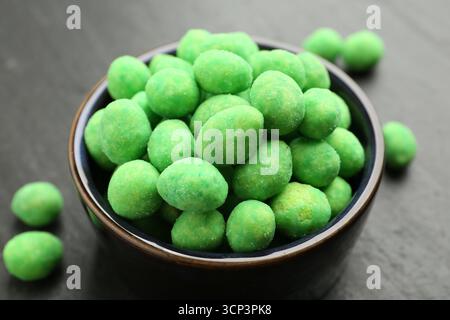 Delicious wasabi coated peanuts and bowl on dark textured table, closeup Stock Photo