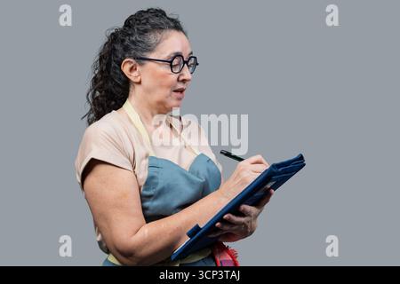 Woman wearing glasses and apron writing notes on a clipboard Stock Photo