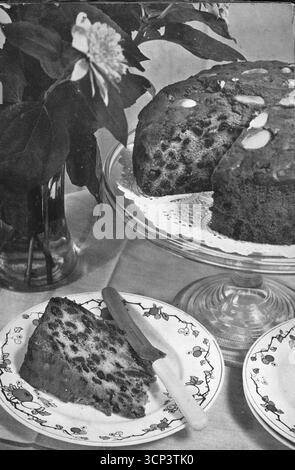 Close up, typical of a 1930s dining table, with a farmhouse cake cooked in a Vulcan oven and resting on a cake dish, and a slice of the said cake on a side plate with a knife. From a printed photograph which originally appeared in the publication, The Vulcan Cook Book, which was published in 1936 by the Vulcan Stove Company of Exeter, England. Stock Photo