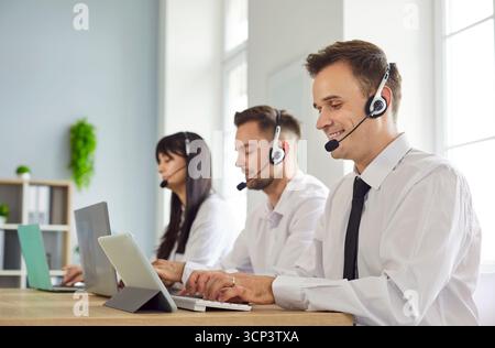 Happy technical support agents in headsets assisting clients at shared office desk Stock Photo