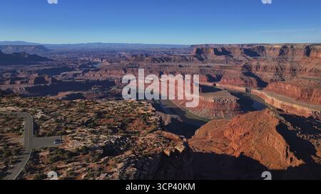 Aerial view of the winding river cutting through the deep canyon, painted in hues of red and brown under a vast blue sky, Moab, Utah, United States. Stock Photo