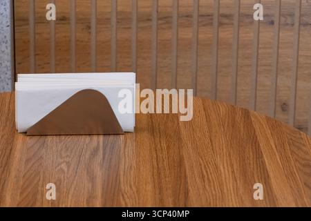Metal napkin holder with white paper napkins on wooden table in modern cafe. Minimalist restaurant detail and clean interior concept Stock Photo