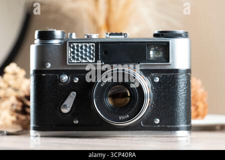 Close-up front view of an old analog film camera placed on a wooden surface, with focus on the lens and body texture. Ideal for themes like vintage ph Stock Photo