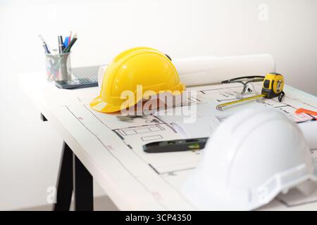 Engineer workspace. Construction helmets and blueprints on a desk for architectural projects. Stock Photo