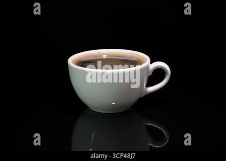 White porcelain cup filled with hot black coffee on glossy black background, minimalistic premium studio shot Stock Photo