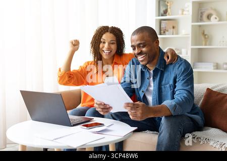 Smiling African American couple celebrating while reading financial documents at home Stock Photo