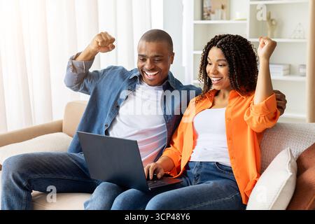 Excited African American couple celebrating success while using laptop together at home Stock Photo