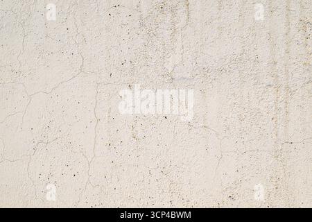 A white wall with a lot of holes and cracks. The wall is very rough and uneven Stock Photo