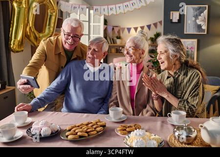 Group of Senior Friends Taking Selfie and Celebrating Birthday Indoors Stock Photo