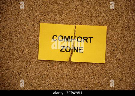A ripped yellow paper note with the words Comfort Zone on it lying on a cork board. Close up. Stock Photo