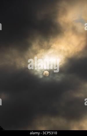 dramatic sky with sun partially hidden by clouds Stock Photo