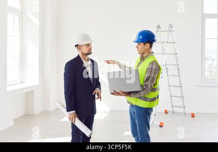 Two men in a helmet with a laptop are discussing a work plan, closeup Stock Photo