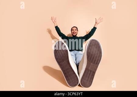 Young man leaning back and gesturing joyfully, wearing casual wear and sitting against a clean background Stock Photo