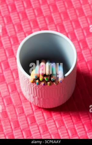 Sharpened pastel colored pencils in a ceramic cup on a colored background for drawing. Macro photography, selective focus. Stock Photo