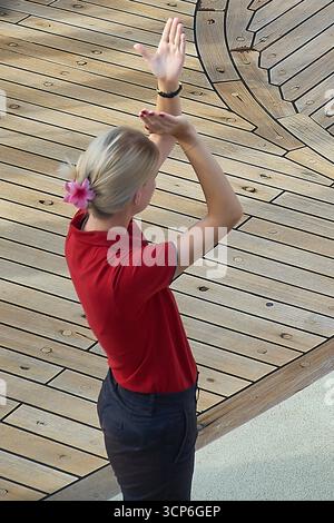 Venice. Italy - September 24, 2025: High angle view of a blonde woman with a flower in her hair, energetically leading a dance or exercise activity on Stock Photo