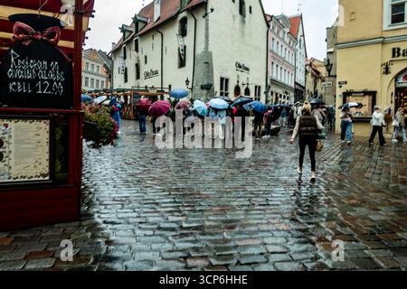 Rainy day in Tallinn Old Town, Estonia, with tourists holding umbrellas walking on cobblestone streets surrounded by historic medieval buildings. Stock Photo
