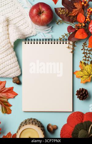 Thanksgiving day background. Falling leaves, notepad, knitted scarf and wooden candle on blue background. Stock Photo