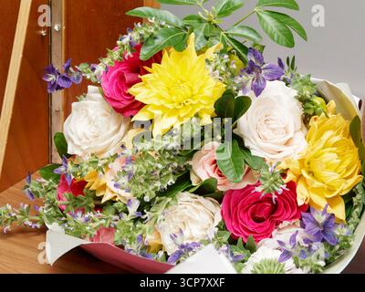 Colorful bouquet with roses, dahlias, and purple flowers, elegantly arranged with foliage on a wooden table, perfect for wedding or celebration. Stock Photo