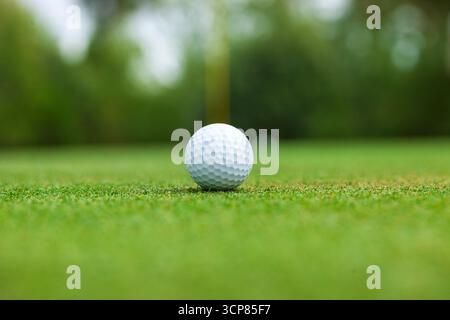 Low angle selective focus view of a golf ball on a green with the flag stick behind Stock Photo