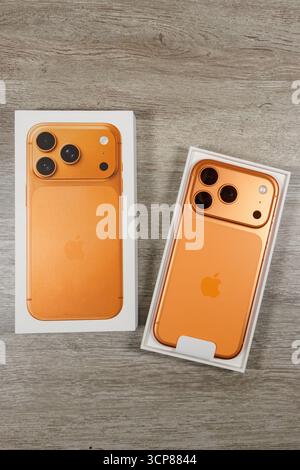 Orange iPhone 17 Pro with its box placed on a wooden surface, displaying the back and camera design of the smartphone Stock Photo