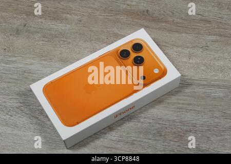 Orange smartphone with three cameras in a box on a wooden surface Stock Photo